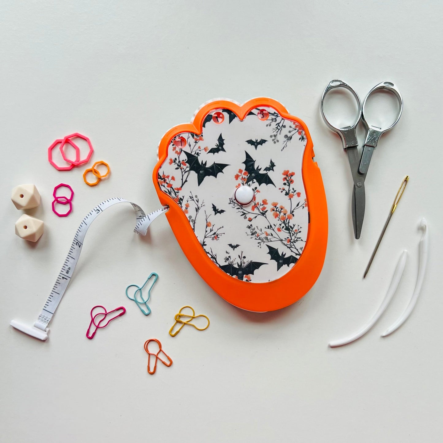 Decorative knitting kit with scissors, measuring tape, and pins on a light gray background