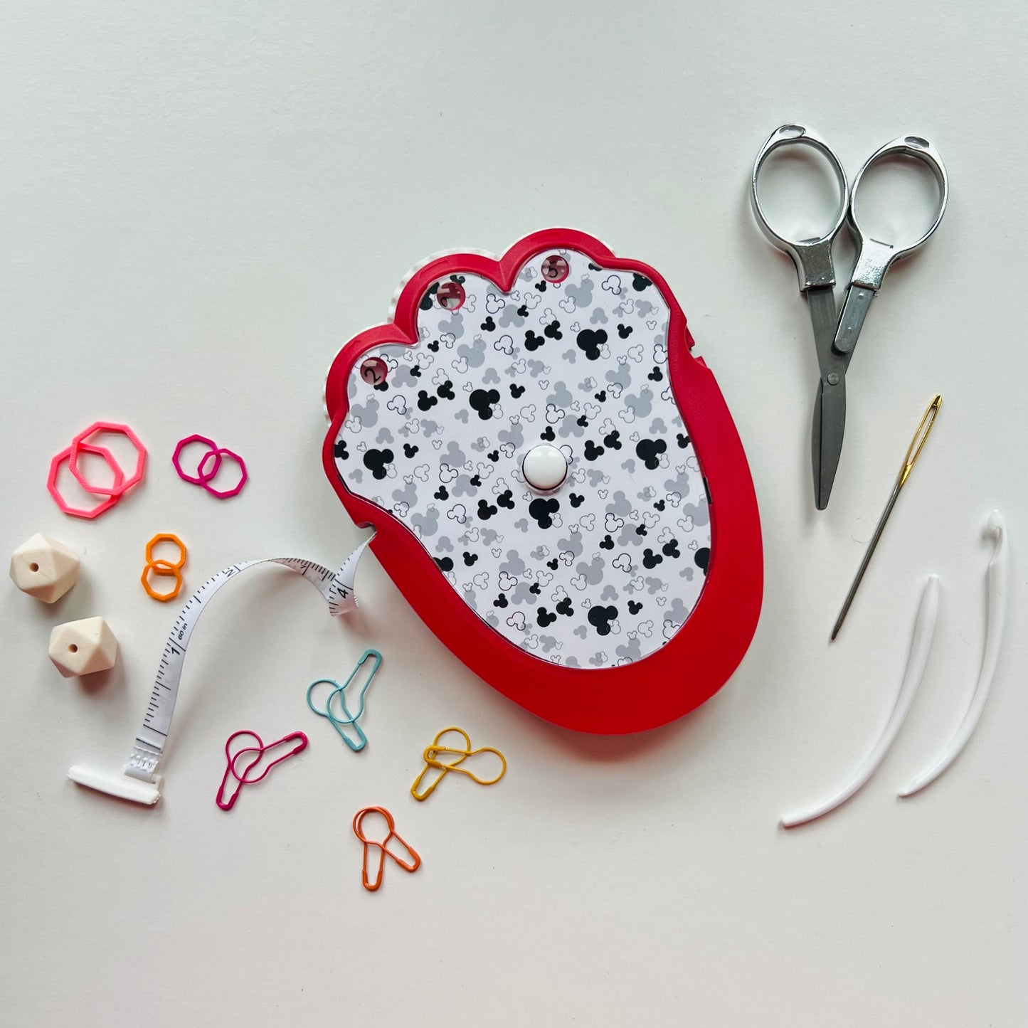 Red knitting kit with scissors, needle, thread, and various knitting tools on a white background