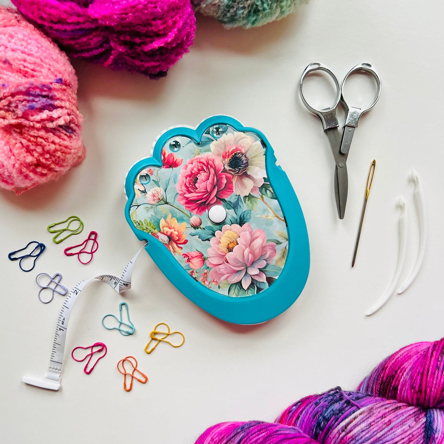 Yarn, scissors, and a floral-patterned case on a white surface