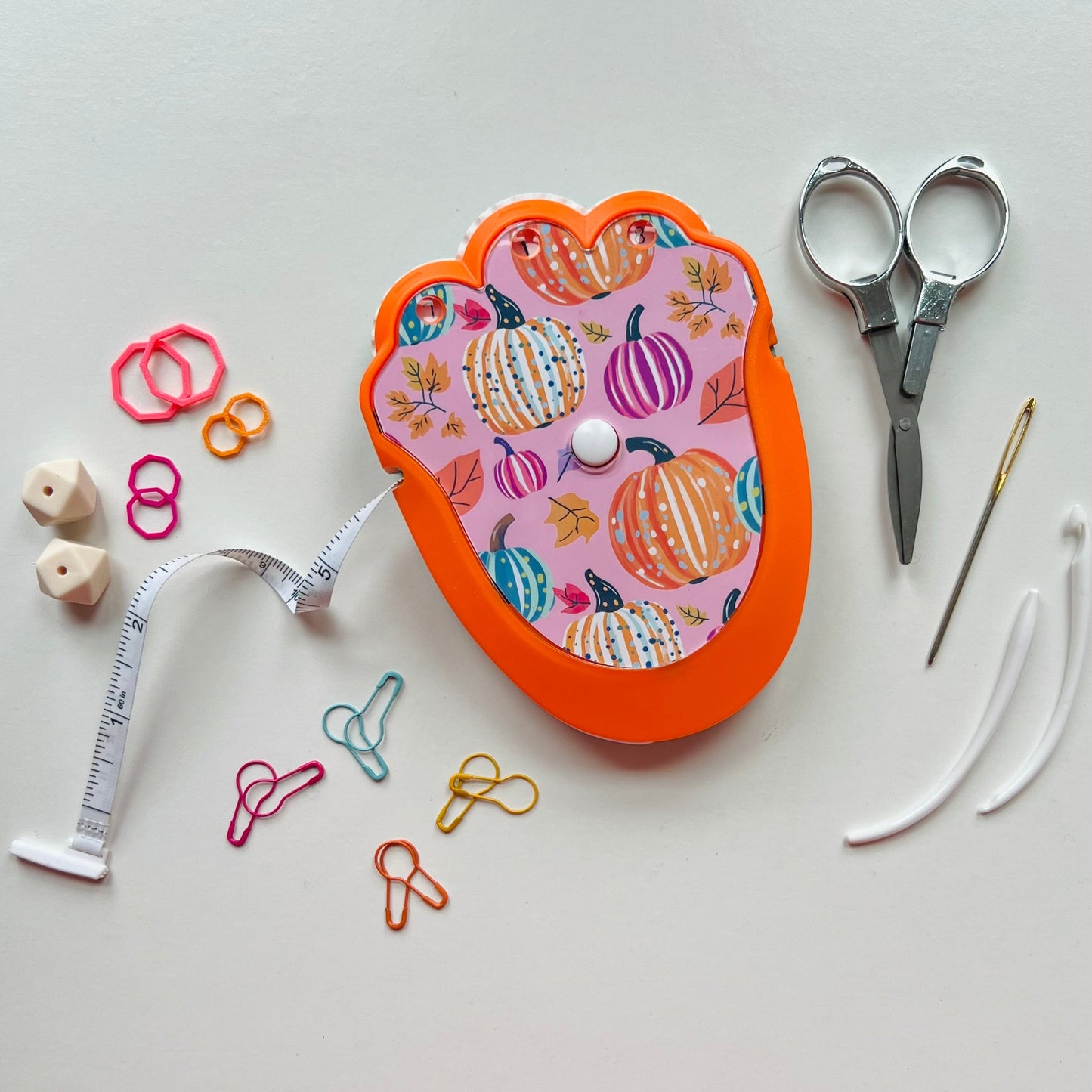 Decorative knitting kit with pumpkins, scissors, measuring tape, and other tools on a light gray background