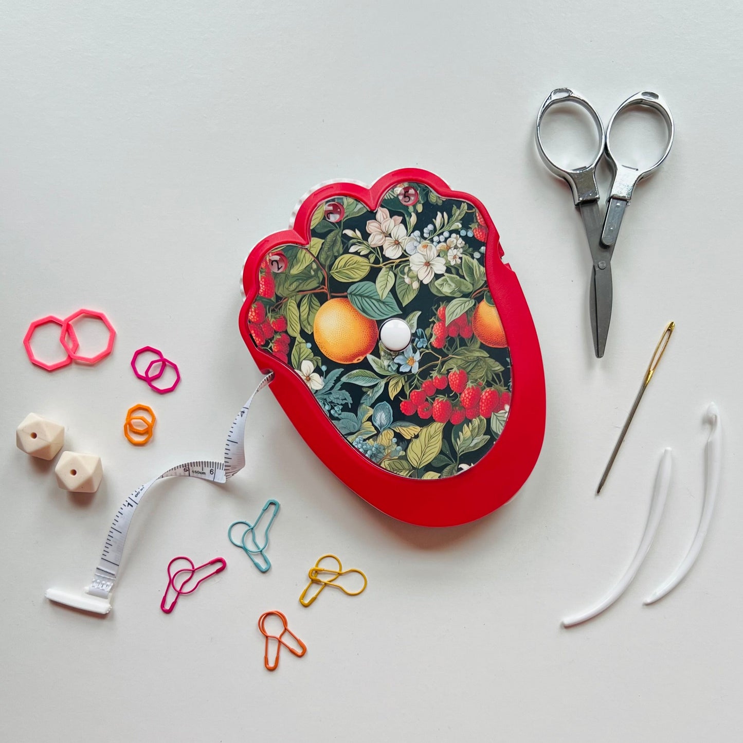 Red floral-patterned case with knitting tools on a light gray background