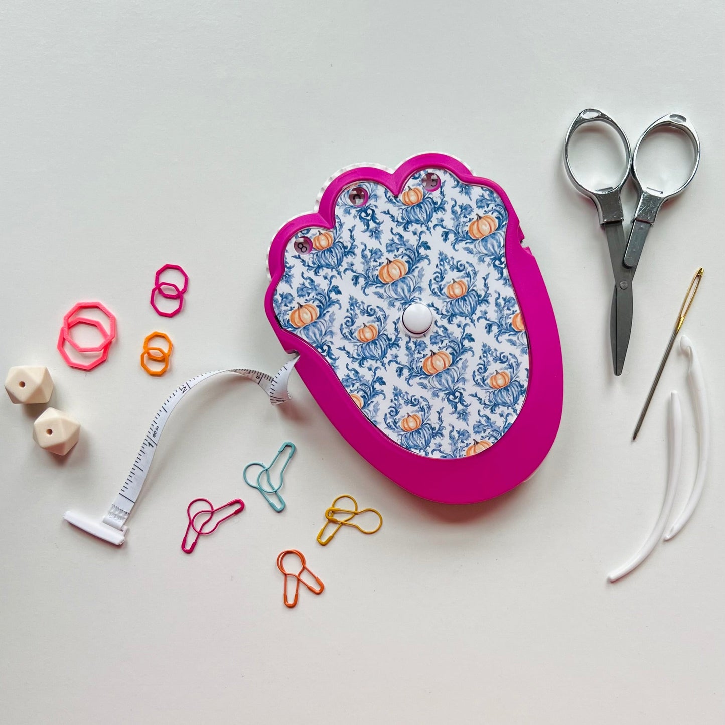 Decorative knitting kit with scissors, measuring tape, and pins on a light background