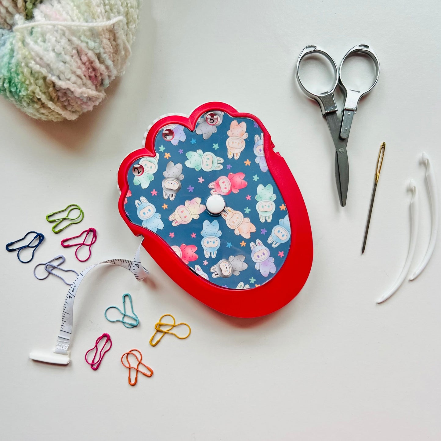 Decorative knit kit with scissors, yarn, and other sewing tools on a white surface
