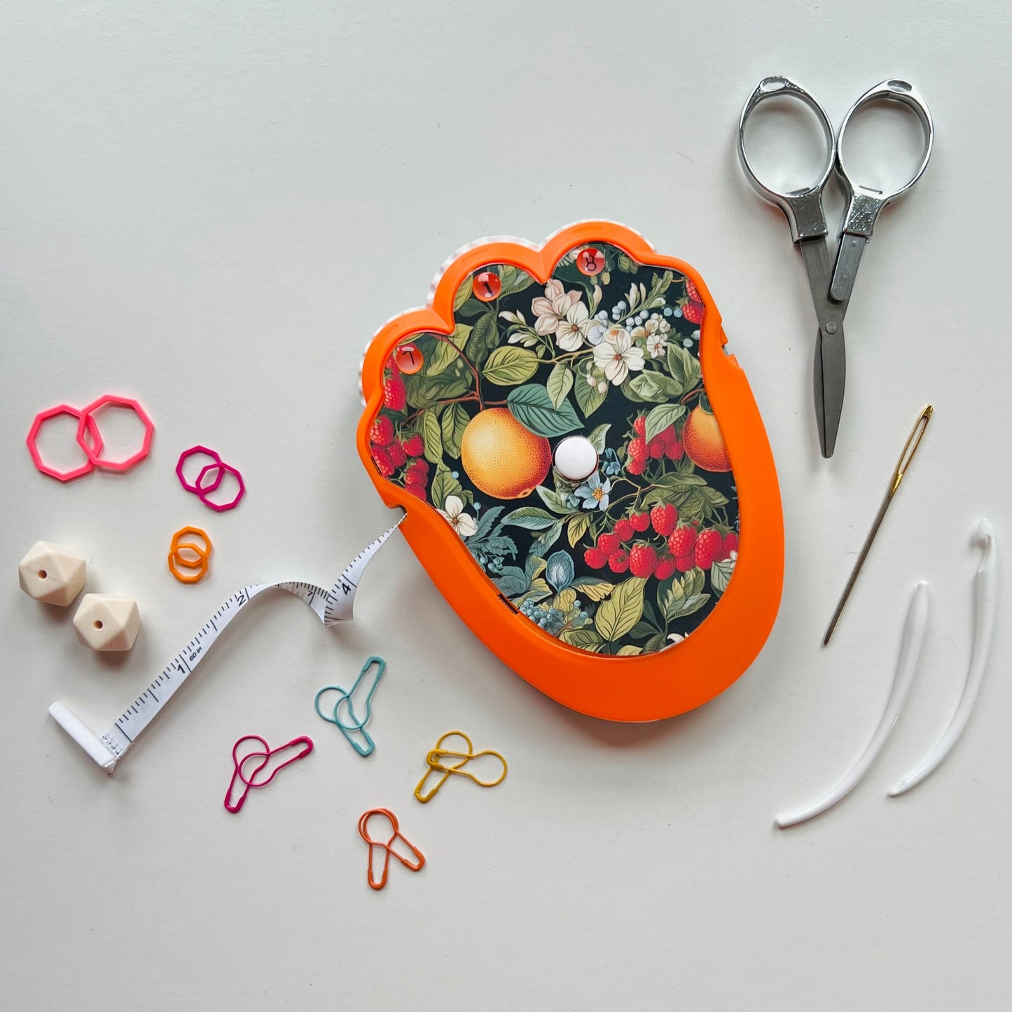 Decorative knitting kit with floral pattern, scissors, measuring tape, and pins on a white background