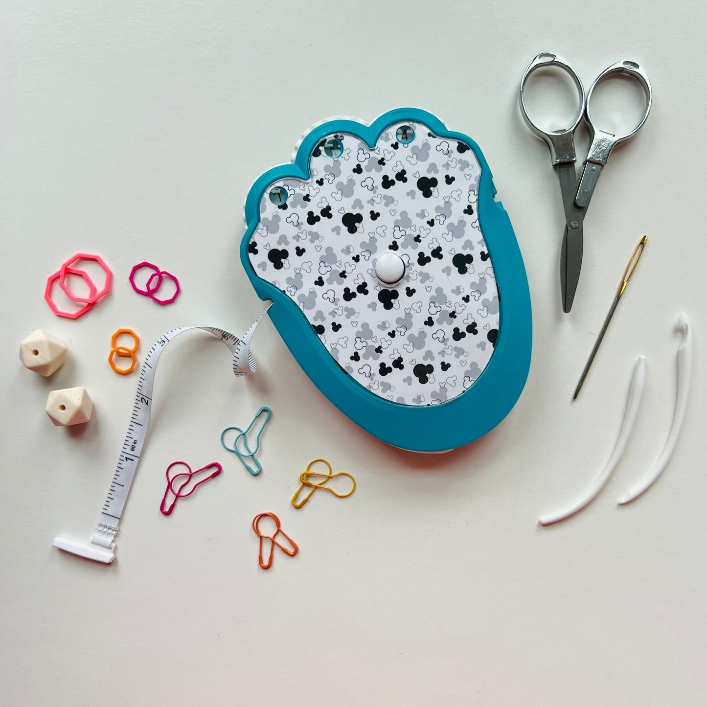 Decorative knitting kit with scissors, measuring tape, and pins on a light gray background