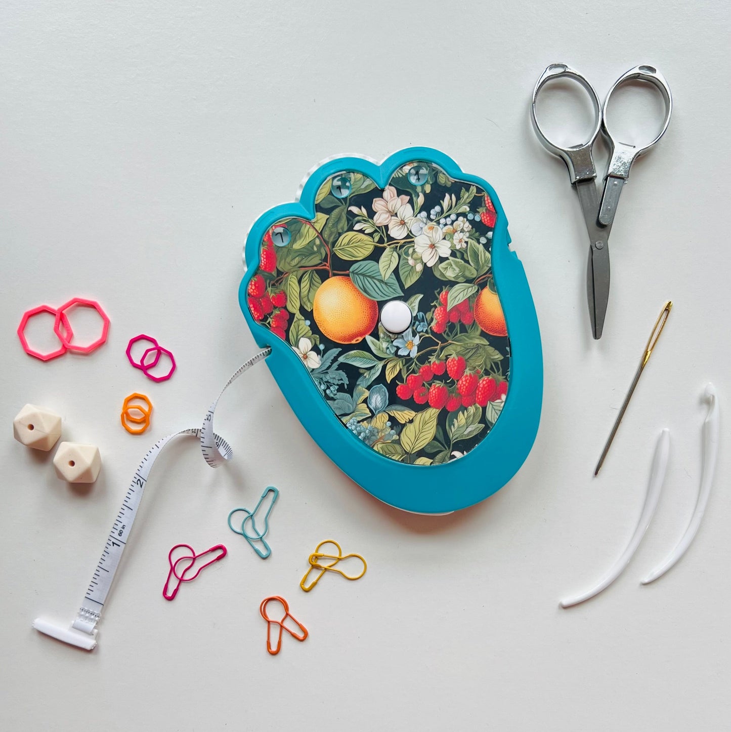 Knitting kit with floral design, scissors, thread, and other knitting tools on a light gray background.