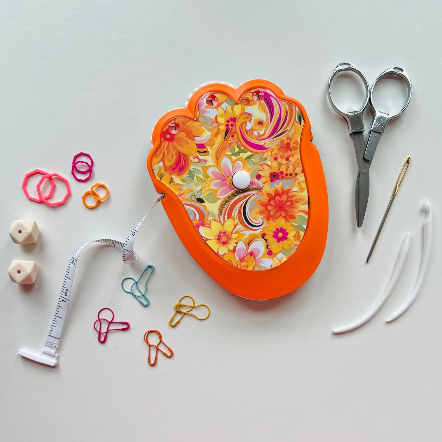 Floral-patterned knitting kit with scissors, measuring tape, and other tools on a white background
