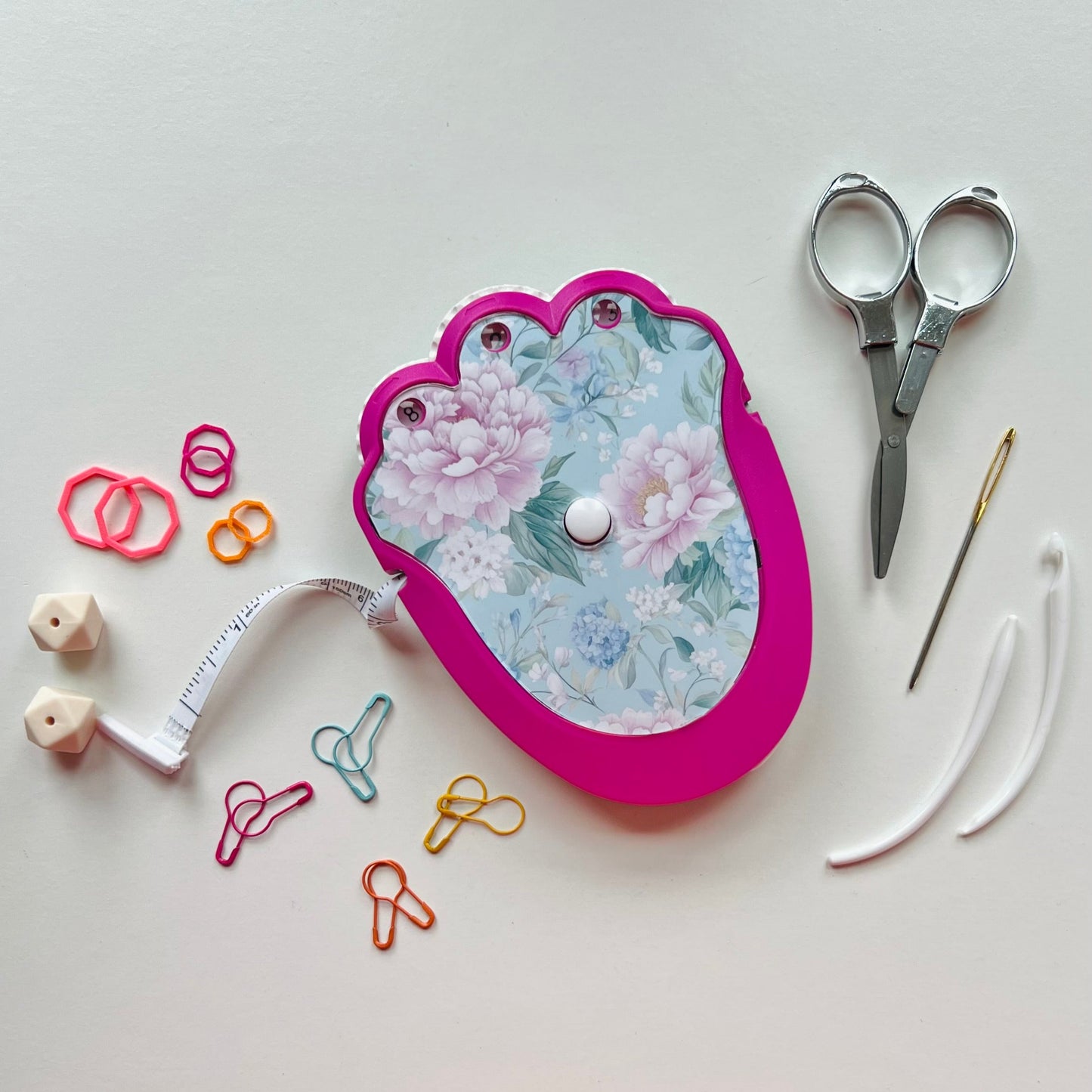 Floral-patterned kitting kit with scissors, measuring tape, and other tools on a white background