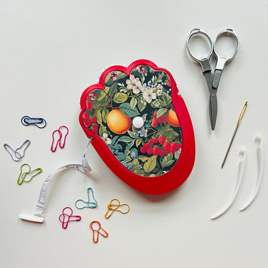 Red floral-patterned crochet kit case with scissors, paper clips, and a needle on a white background