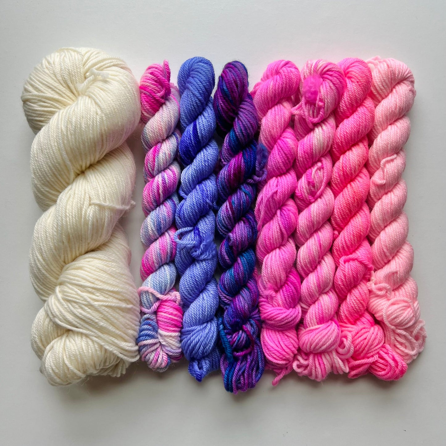 Three skeins of yarn in white, pink, and blue on a light gray background