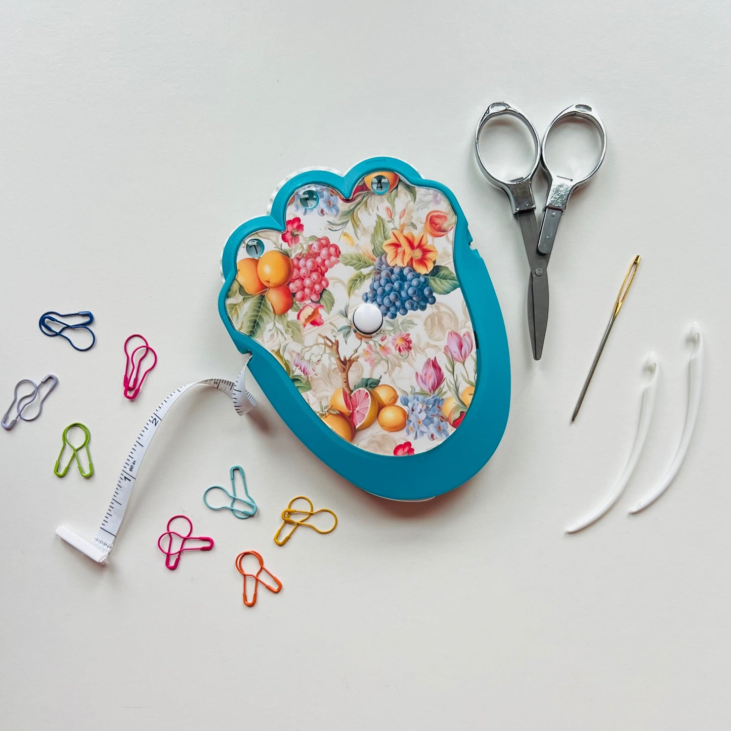 Floral-patterned crocheting kit with scissors, measuring tape, and pins on a white background