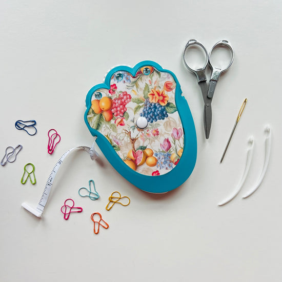Floral-patterned crocheting kit with scissors, measuring tape, and pins on a white background