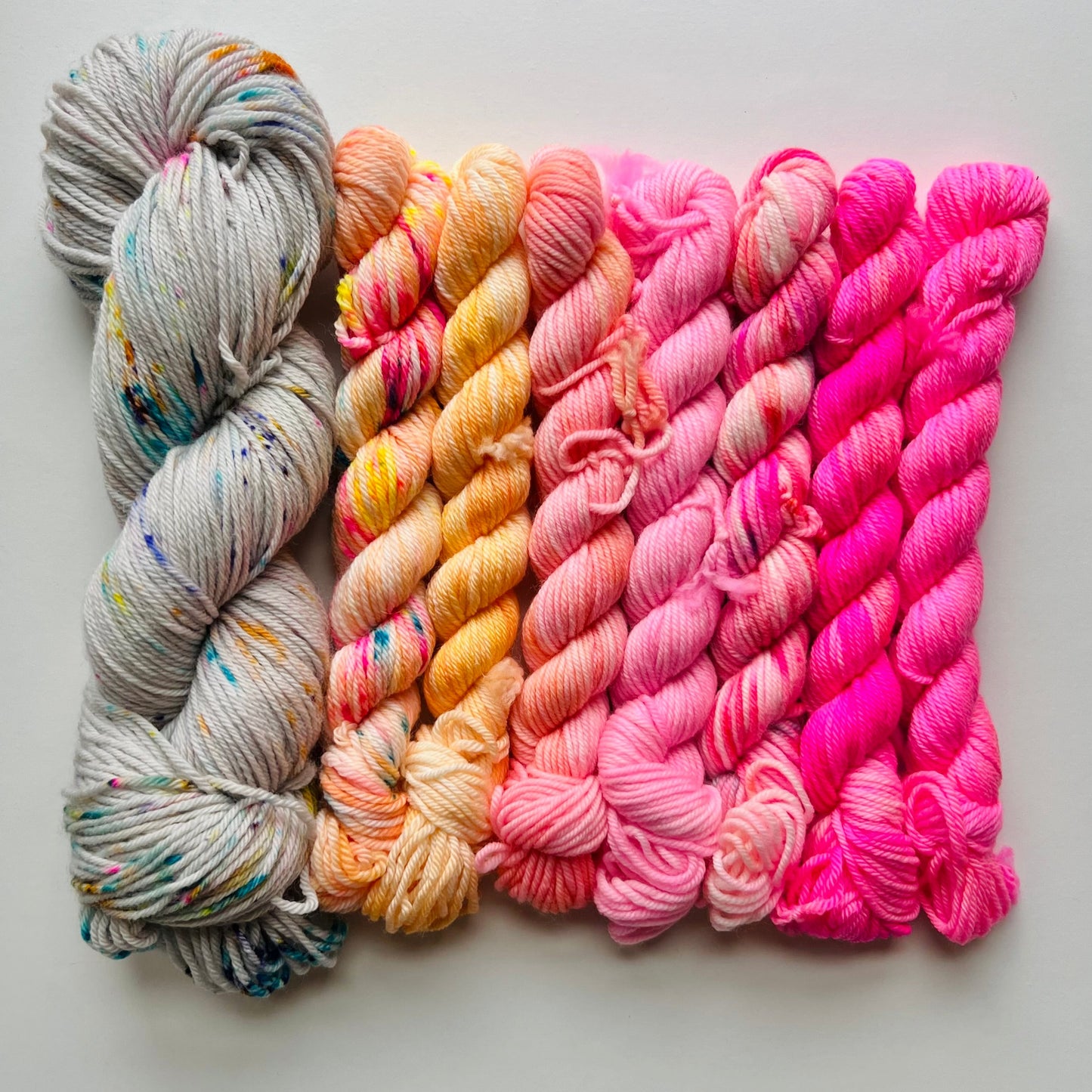 mini skeins of yarn in gray, orange, and pink on a light gray background
