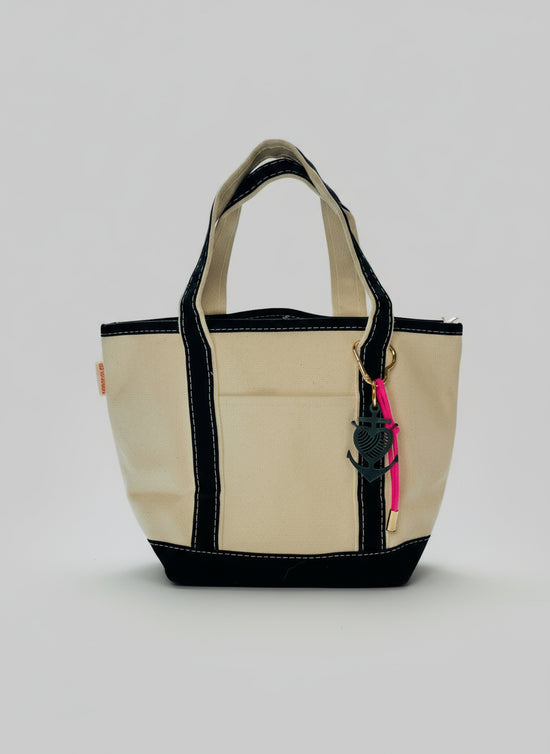Beige tote bag with black trim on a white surface, with a blurred background of a house and person.