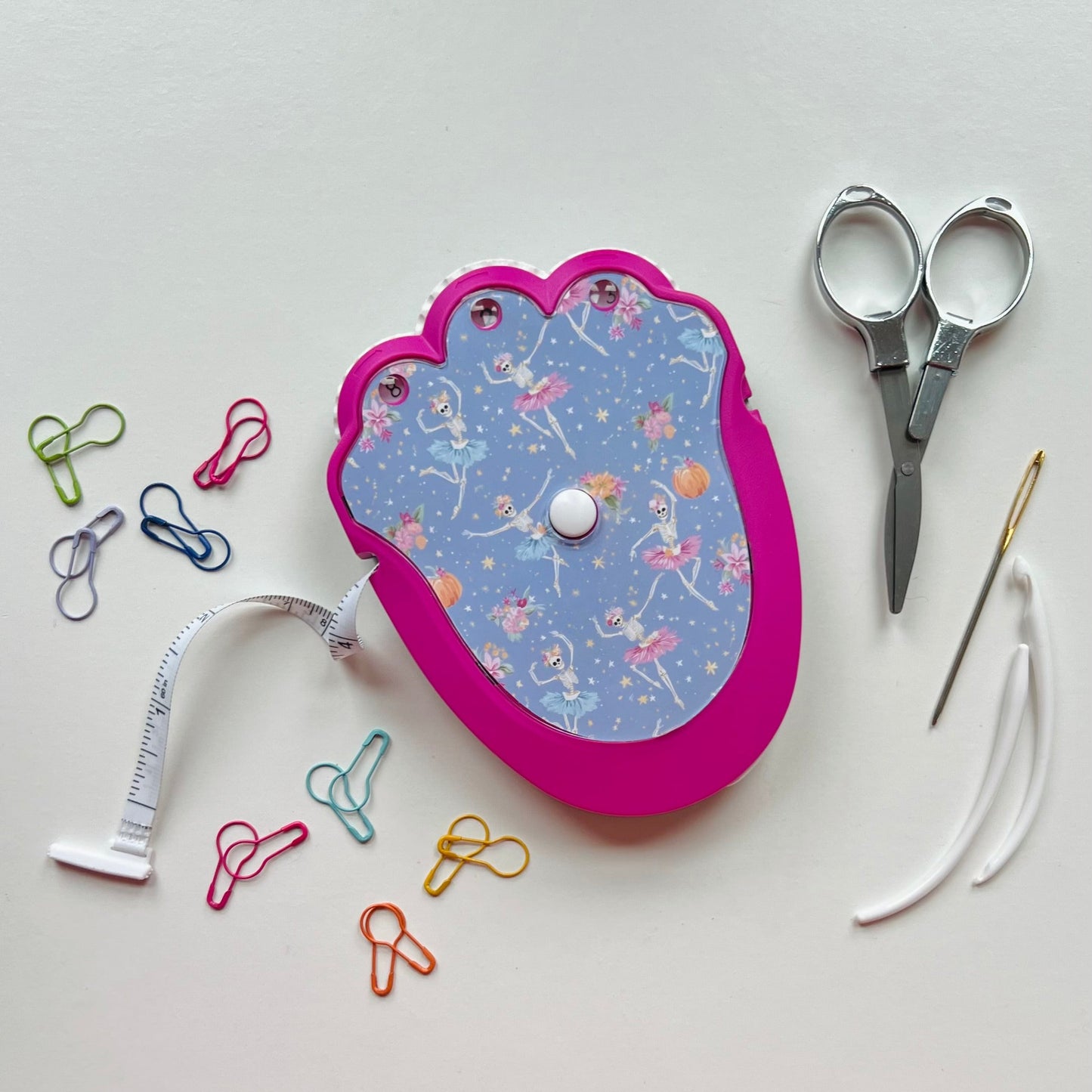 Pink and blue crocheting kit with scissors, needle, and pins on a white background