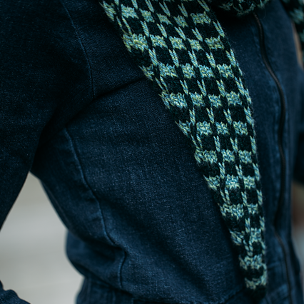 Person wearing a dark blue outfit with a patterned scarf, showing tattoos on the hand.
