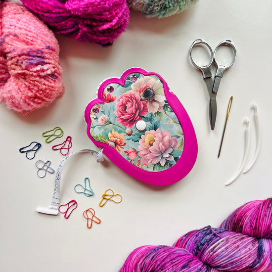 Colorful yarn skeins, a floral-patterned tape measure, scissors, and knitting needles on a white background.