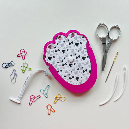 crochet kit with patterned top, scissors, measuring tape, and colorful pins on a light gray background