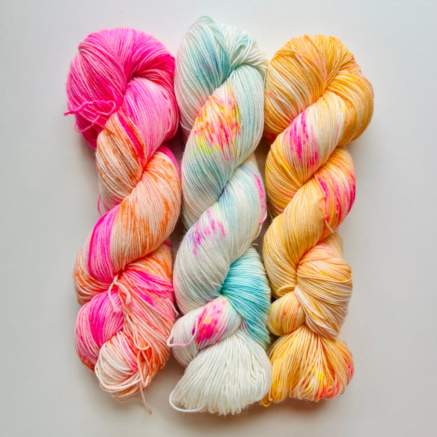 three skeins of colorful yarn in pink, orange, blue, and yellow on a light gray background