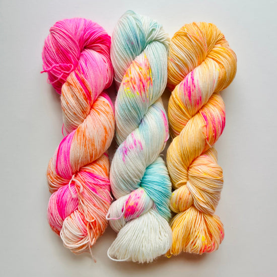 three skeins of colorful yarn in pink, orange, blue, and yellow on a light gray background