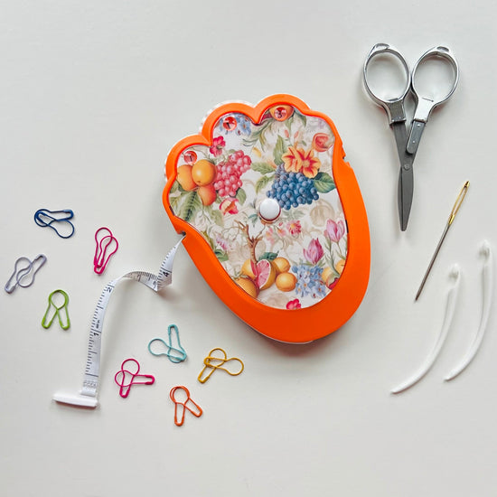 Decorative crocheting kit with floral design, scissors, measuring tape, and paper clips on a light gray background