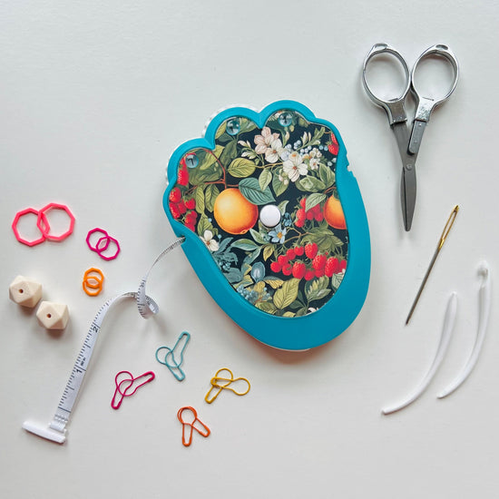 Knitting kit with floral design, scissors, thread, and other knitting tools on a light gray background.
