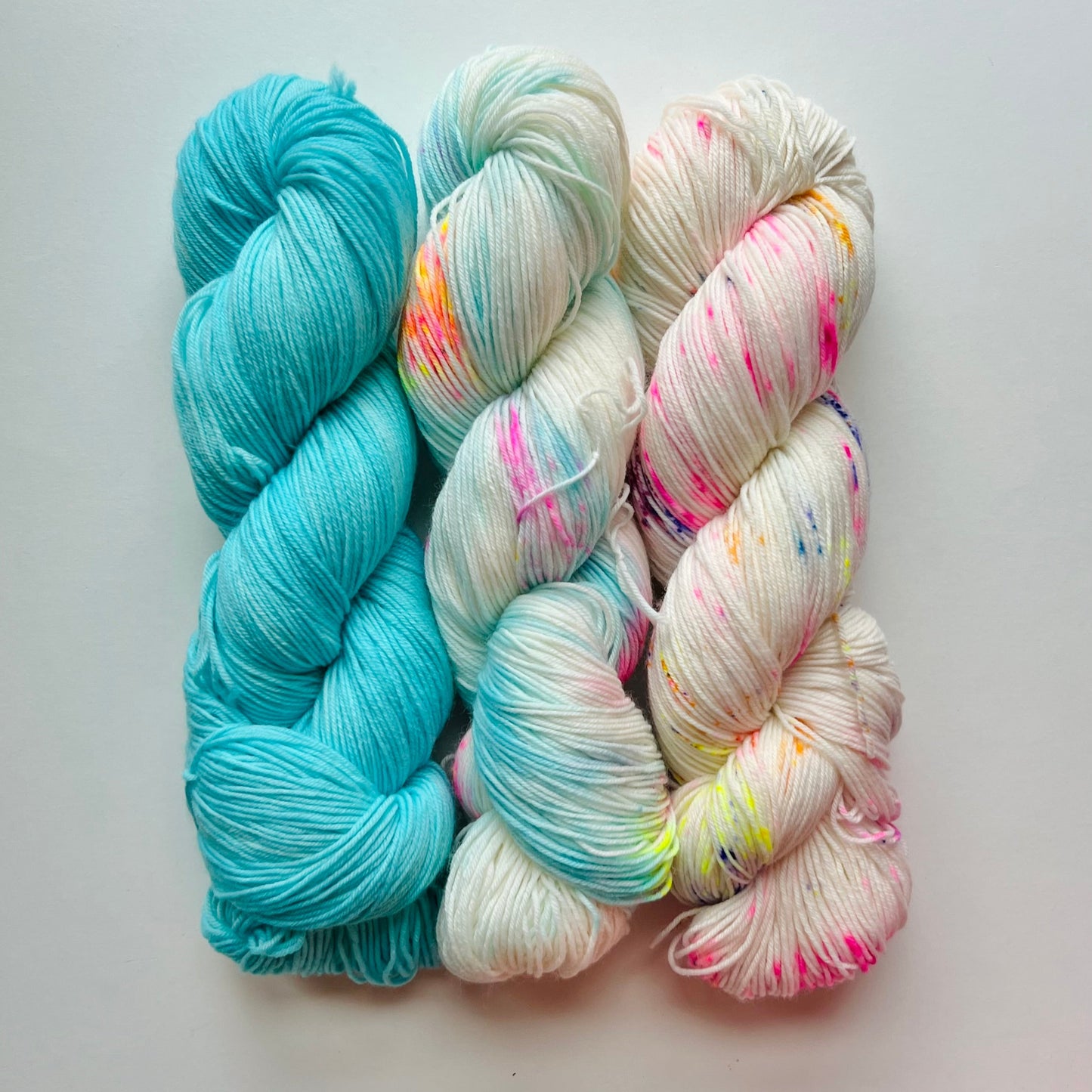 Three skeins of yarn in blue, white, and multicolor on a light gray background