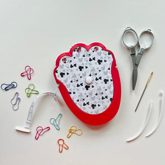 Crocheting tool kit with scissors, needle, and measuring tape on a white background
