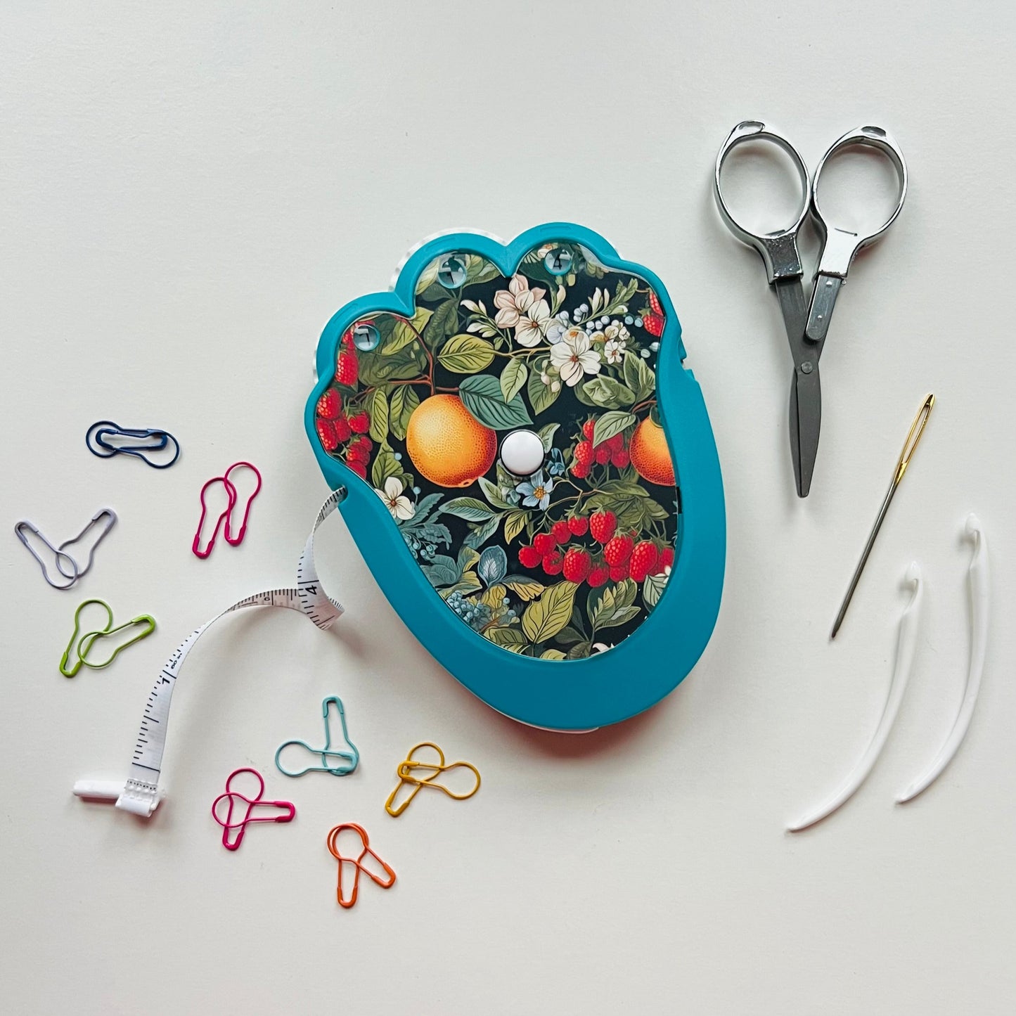 Decorative crocheting kit with floral design, scissors, needle, thread, and paperclips on a white background