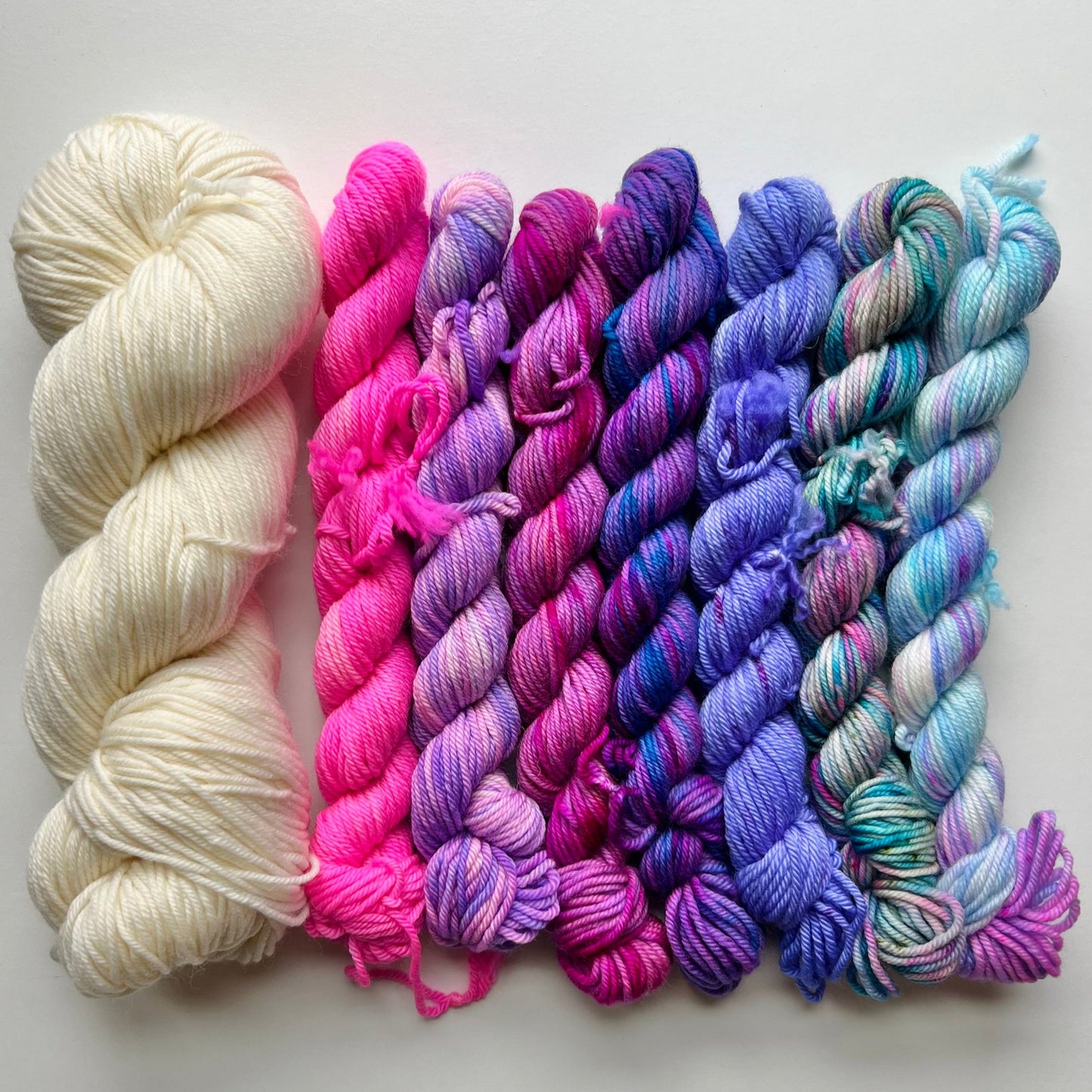 mini skeins of yarn in white, pink, and multicolor on a light gray background