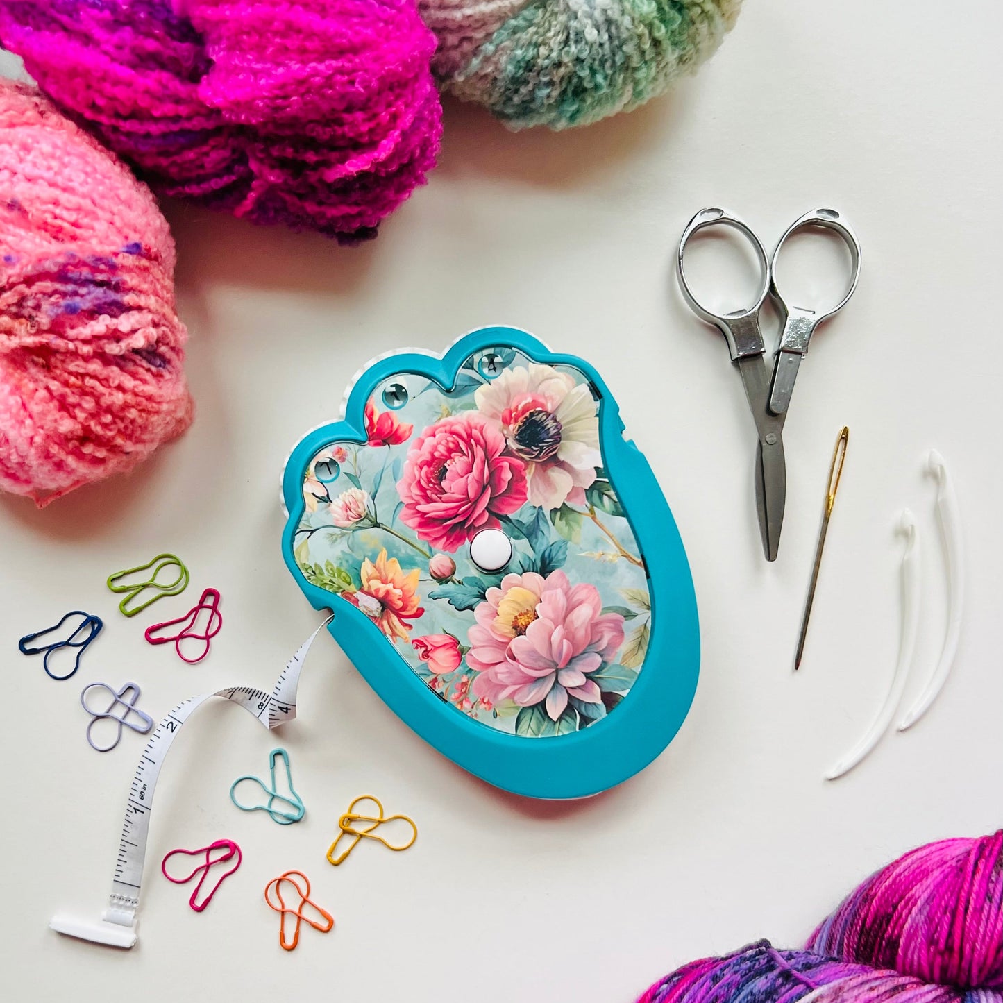 Yarn balls, floral-patterned case, scissors, and knitting needles on a white surface