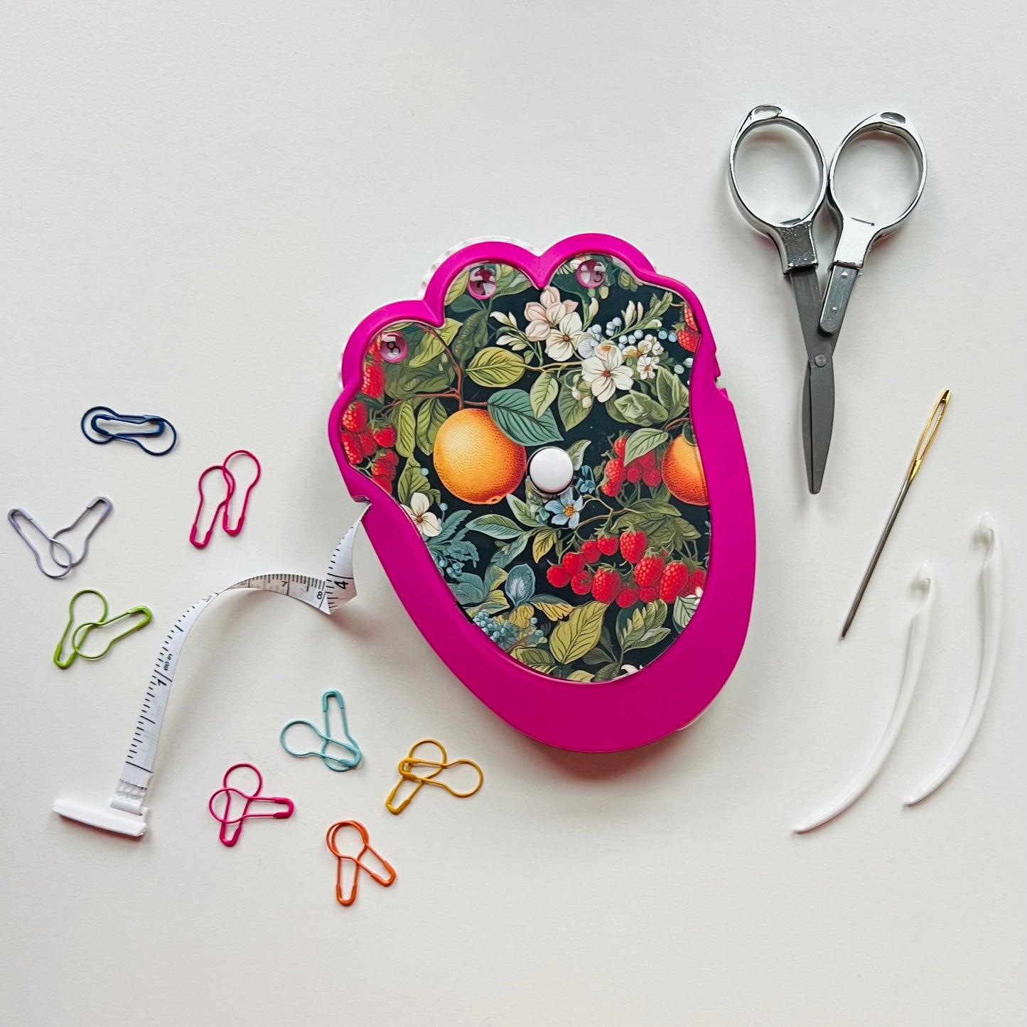 Floral-patterned crocheting kit with scissors, measuring tape, and paperclips on a white background