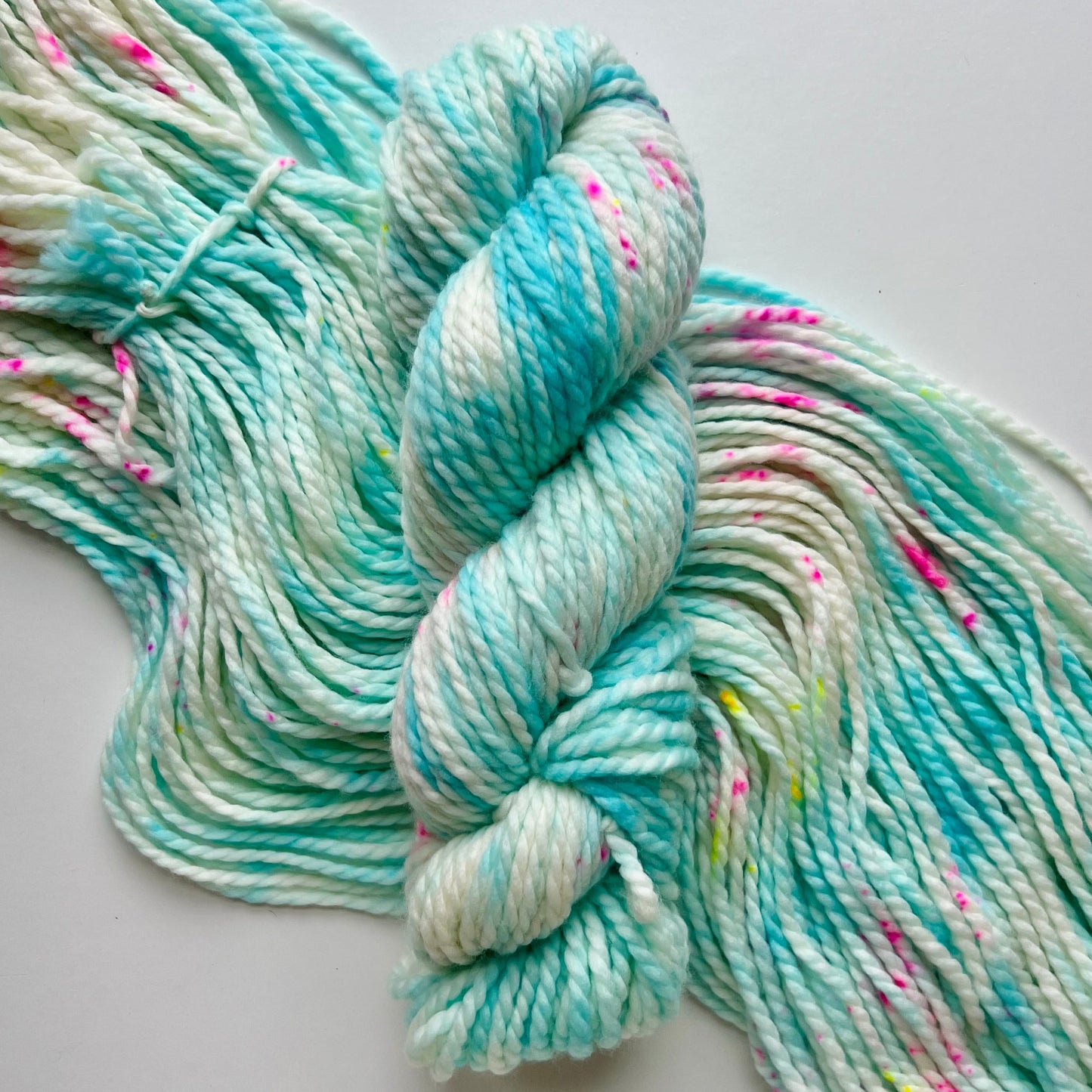 Turquoise and white skein of yarn with speckles on a light gray background